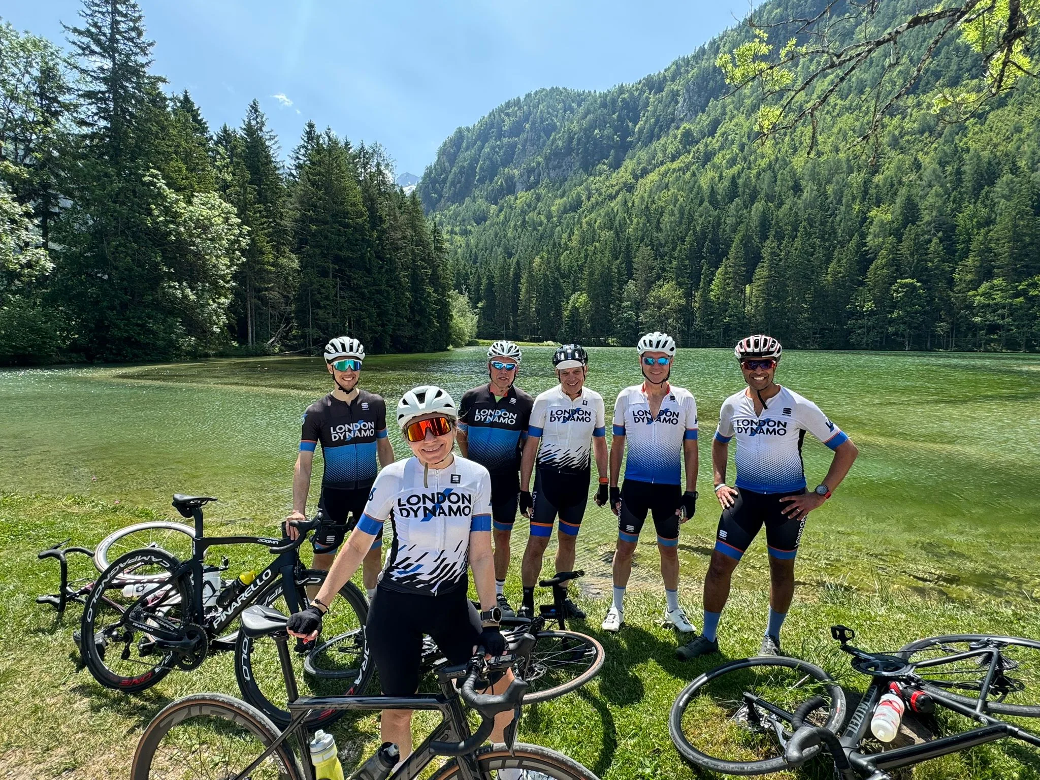 London Dynamo mixed group of cyclists standing next to a lake in the forested mountains of Slovenia.