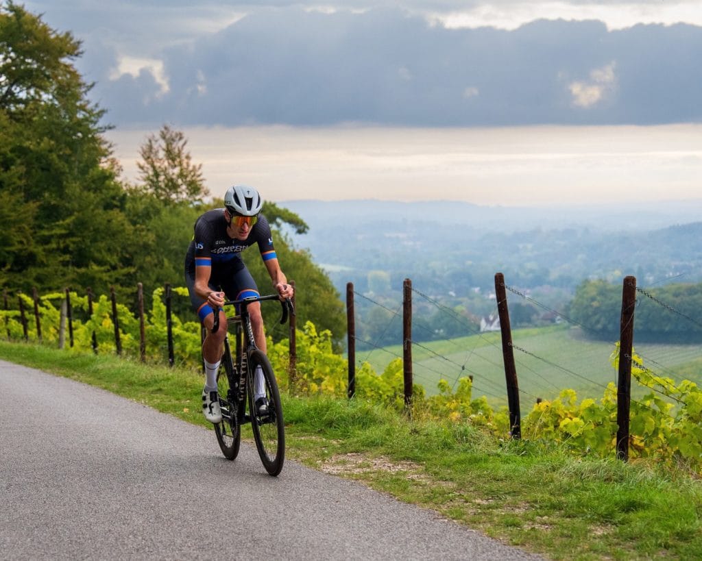 A London Dynamo rider climbing a country lane with the Surrey Hills behind